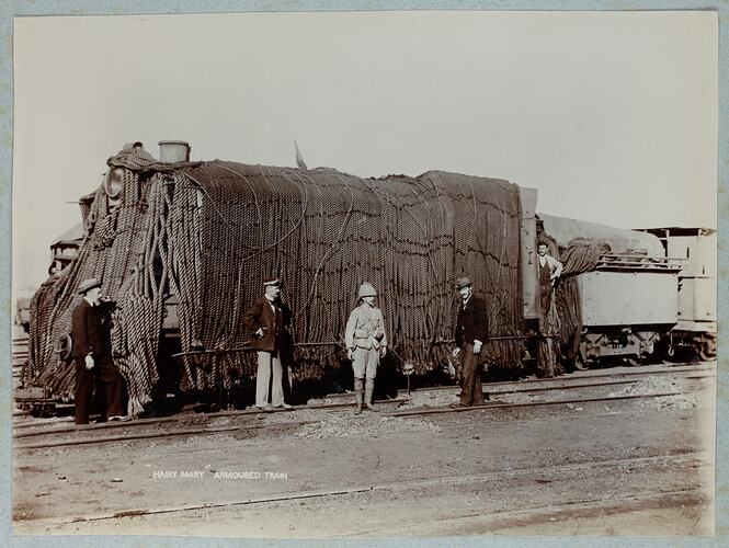 Five men standing in front of train engine covered in heavy armour chain.