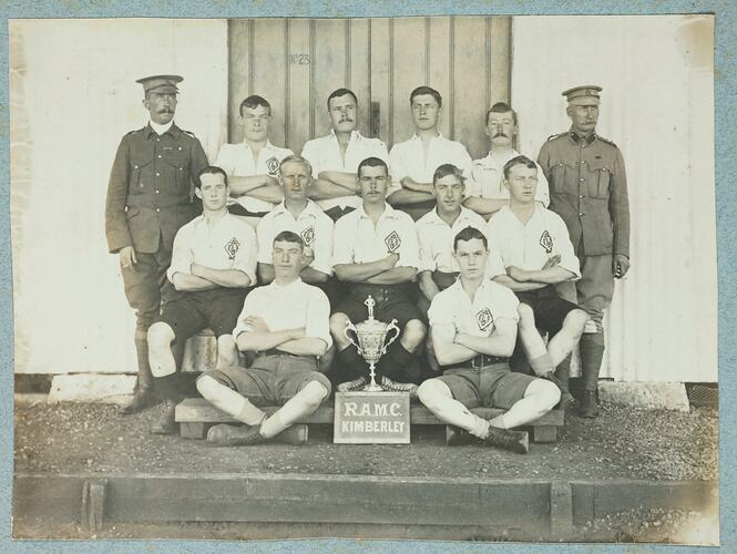 Group portrait of thirteen men, with eleven wearing sports clothing and two wearing military uniforms.