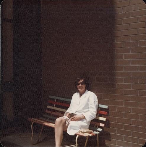 Woman in lab coat seated on bench outside building.