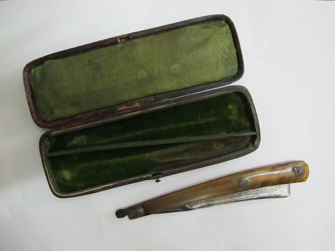 Cut-throat razor next to green-lined box, open