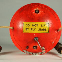 Red cylindrical container with two electrical cords at one end.