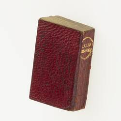 Miniature red book with gold writing on spine.