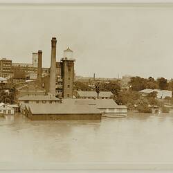 Flooded riverscape with factory buildings and trees partially submerged.