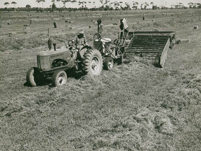A man driving a tractor towing a Pickup baler in a field.
