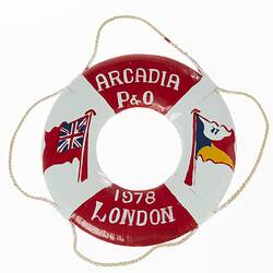 Red and white miniature lifebuoy with two flags painted on each side. Rope around rim.