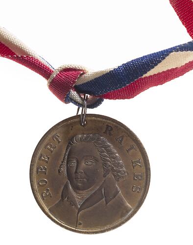 Round copper medal with with three-quarter bust of male facing left. Text around. Suspended from ribbon.