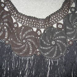 Detail of black crocheted shawl. Top edge features ring of circles made of twirls.