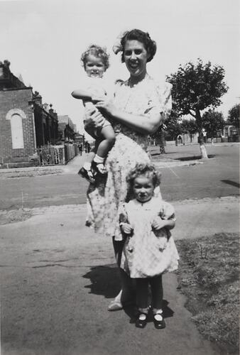 Woman with two children standing on street.