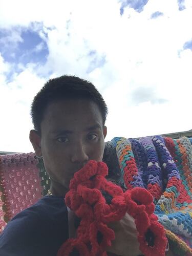 Man holding crocheted poppies near face. Crocheted blanket behind.