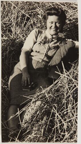 Smiling woman holding a camera and sitting in what appears to be a bundle of hay.