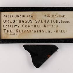 Rectangular black framed label with black text on cream card.