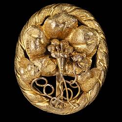 Oval decorative gold brooch containing a flower inside a larger flower, all within an oval border entwined with gold ribbon.