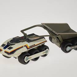 Cream six-wheeled toy truck with grey two-wheeled trailer. Stickers on sides. Left profile.