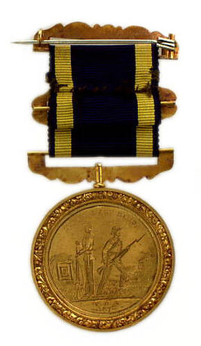 Round, gold coloured medal with two men holding long rifles, blue and yellow ribbon attached.