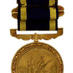 Round, gold coloured medal with two men holding long rifles, blue and yellow ribbon attached.
