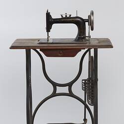 Sewing machine fitted to a metal frame with a wooden bench.