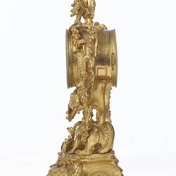 Elaborately decorated gold mantel clock. Left profile.