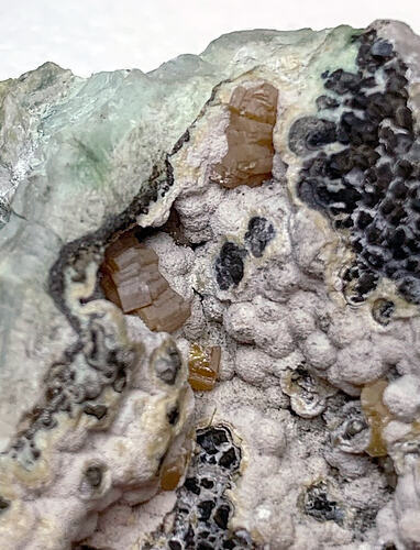 Variouos shaped green, pink, black and brown minerals growing together.