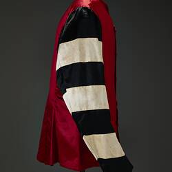 Profile of red riding jacket with red buttons. Black and white hoops on sleeves. Short stand up red collar. Black background.