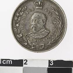 Round silver coloured medal with profile of man with crown above, surrounded by text and wreath,