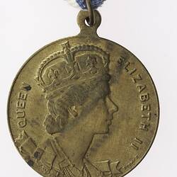 Round medal with profile of crowned woman and text surrounding, with red, white and blue ribbon attached.