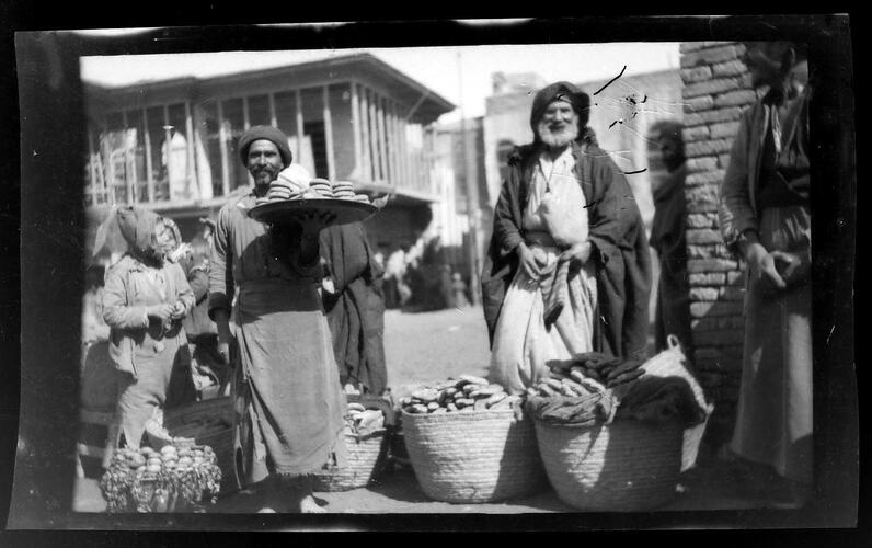 Group of men on street with baskets of food produce.
