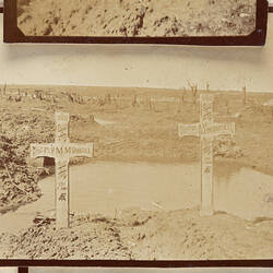 Two crosses covered in writing with puddle and barren landscape behind.