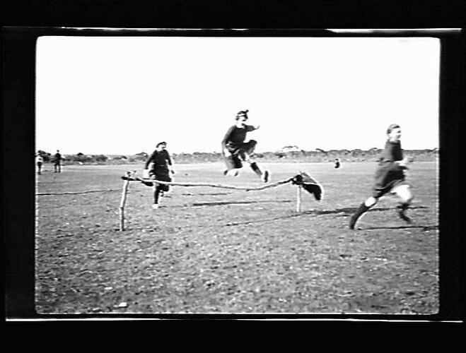 Grainy black and white photo of women jumping over a hurdle.