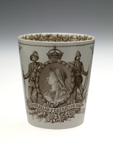 Cream earthenware beaker with sepia floral patterning. Two soldiers frame cameo of Queen Victoria.