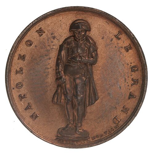 Round medal with male statue. Text around.