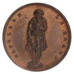 Round medal with male statue. Text around.