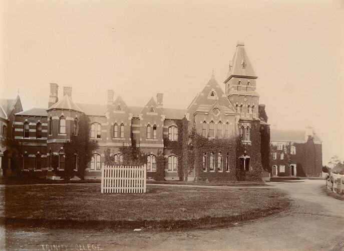 Exterior of large, two-storey stone building with multiple gables and large tower above front entrance. Circular lawn and sweeping driveway.