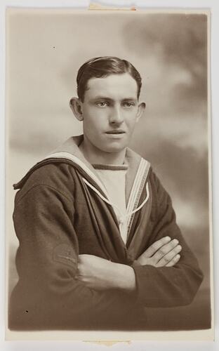 Studio portrait of a man in Navy uniform with crossed arms.