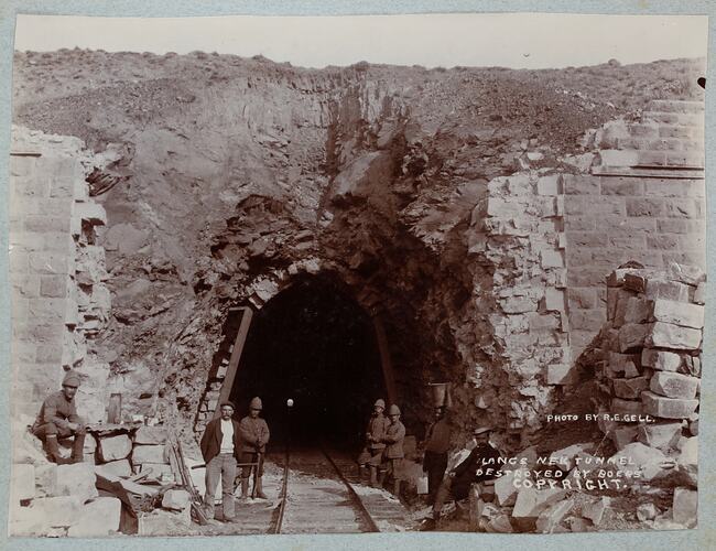 Seven men standing in front of damaged train tunnel entrance.