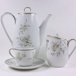 China coffee pot, milk and sugar jugs, cup and saucer, white with delicate rose pattern.