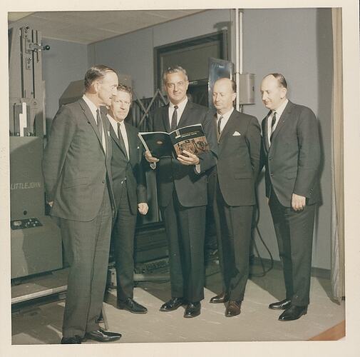 Five men in suits, one holding a magazine.