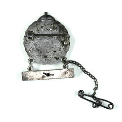 Back of circular badge with bar and pin below.