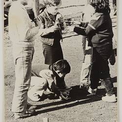 A group of boys in a playground playing 'Marbles'.
