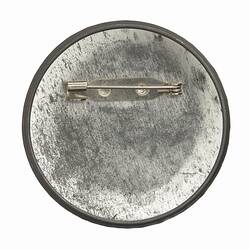 Reverse of round metal badge with horizontal pin.