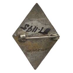 Back of diamond-shaped metal lapel pin with metallic silver back and lockable pin.