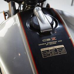 Silver motor cycle. Black tank detail, top view. Model type and safety in gold lettering.