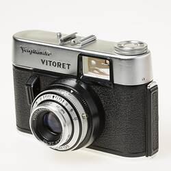 Black camera, metal top section and lens. Front angle view.