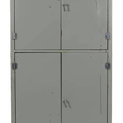 Grey metal cabinet, four closed doors. Vent hole at base.