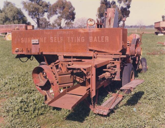 Self Tying Baler in a field with other farm equipment in background.