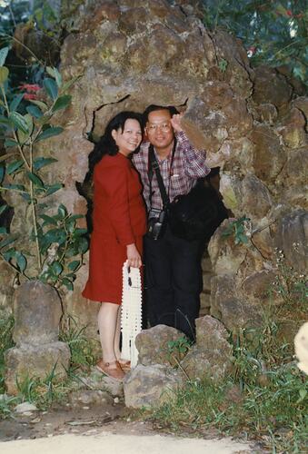 Woman wearing red dress suit and man stand at cave entrance.