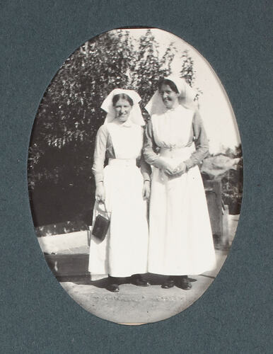Two nurses with camera next to shrubbery.