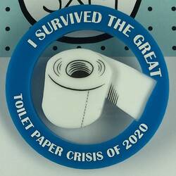 Circular plastic badge with illustration of toilet paper.