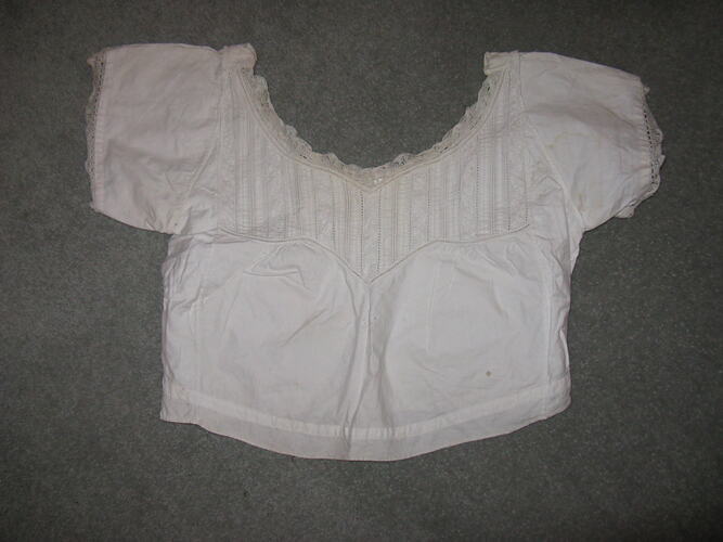 White cotton camisole with short sleeves and neckline edged with lace. AD in centre.