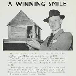 Man with hat holding a model of the McKay Farm Smithy