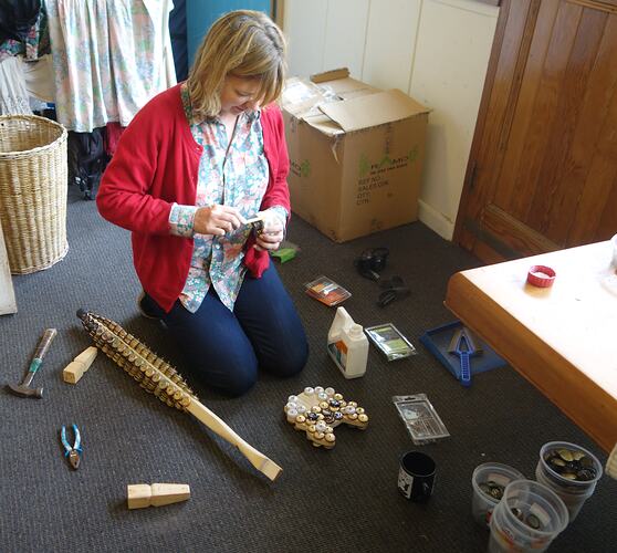 Kneeling woman working with bottle tops and other lagerphone components.